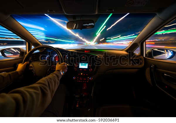hands on the wheel a car moves at fast speed\
at the night. Blured road with lights with car on high speed. Car\
speed night drive on the road in\
city