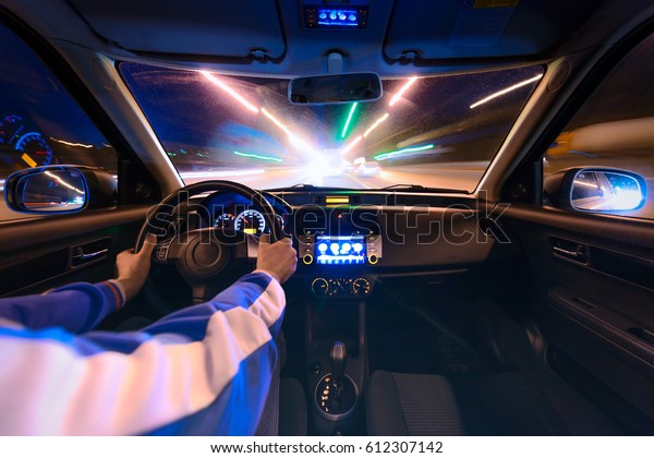 hands on the wheel a
car moves at fast speed at the night. Blured road with lights with
car on high speed