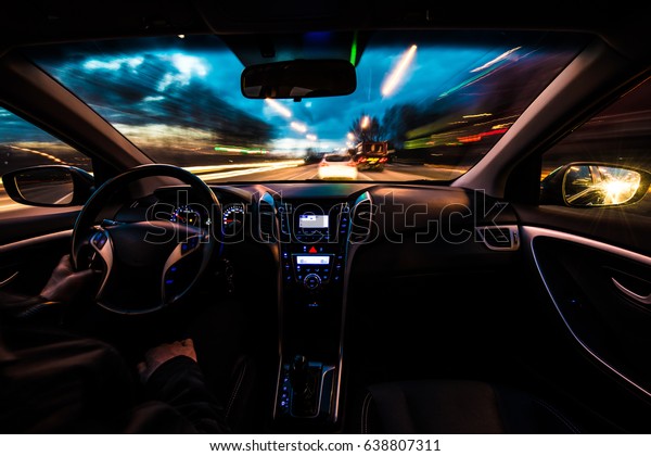 Hands on the wheel, the car\
is moving at a fast speed at nightfall. Blurred road with lights\
with a car at high speed. Instagram Effects with noise and\
toning