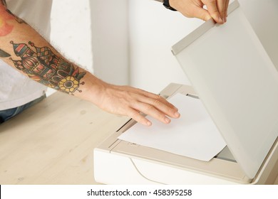 Hands open a scanner tray and put paper sheet to scan a document inside multifunctional electronic device, isolated on white wooden table,