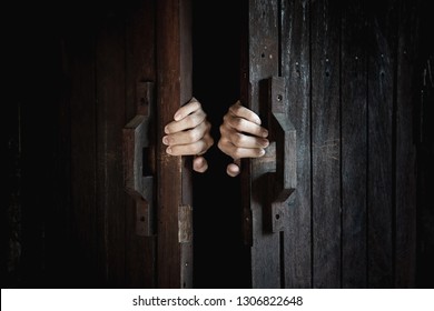 Hands open the wooden door from the inside of the dark room.