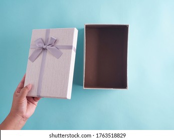 Hands Opening Gift Box On A Light Blue Background. Top View.