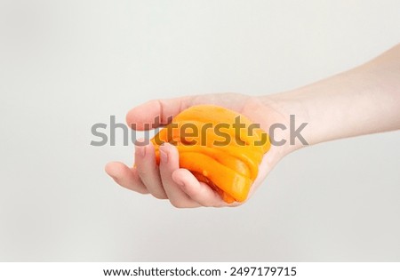 Hands with orange slime close up. A child in a white t-shirt stretching slime. Trendy liquid toy sticks to hands. kids hands playing slime toy. soft dough