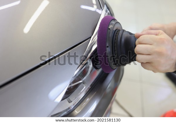 Hands with orbital polisher in car workshop polishing\
headlight of car