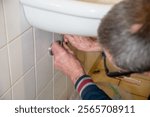 Hands of owner using wrench to repair sink in tiled bathroom, DIY sink installation concept at home,