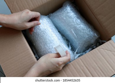 Woman’s hands packing fragile items with plastic air bubble wrapped and adhesive tape and putting in a brown cardboard parcel box.