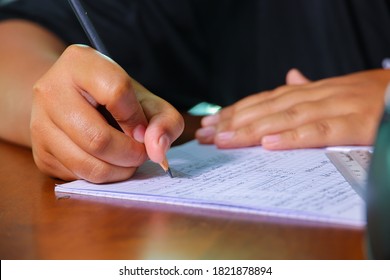 Hände mit Bleistift schreiben in einem Papierbuch. Der junge malaysische Junge sitzt auf einem Tisch und beendet seine Hausarbeit. Malaysischer Student während seines Studiums. Asiatischer Teenager in der Schule, Nahaufnahme beim Händeschreiben