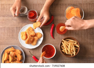 Hands Of People Eating Fast Food Snacks With Chili Sauce At Wooden Table, Top View