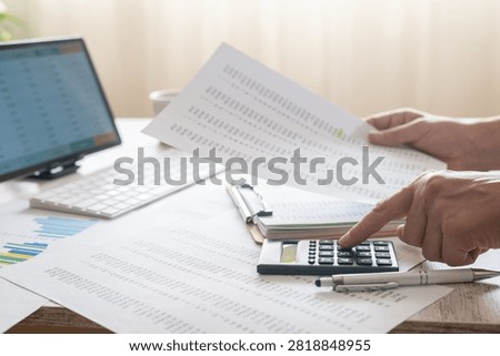 Hands performing essential accounting tasks, using a calculator and reviewing financial documents and data on a computer screen, signifying meticulous budgeting and reporting