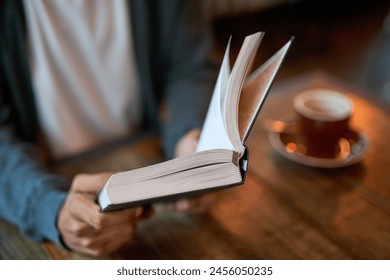 Hands, person and book with coffee at cafe in table for reading novel or story for knowledge. Restaurant, literature and break in desk to chill, relax and lunch with notebook or journal with notes - Powered by Shutterstock