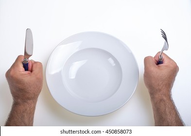 hands of a person holding a knife and fork and claim something to put in the empty plate that has in front of him