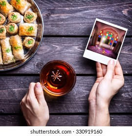 Hands with photo of Rajasthan palace and badyan tea near Turkish baklava on wooden background  