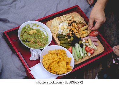 Hands Picking Food From A Tray With Guacamole (avocado And Tomato), Nachos And A Table With Pickles, Celery, Strawberries, Olives, Cheese, Hearts Of Palm, Cookies, Nuts And Ham