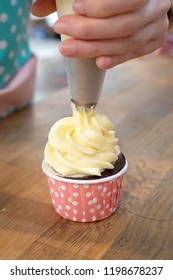 Hands Piping Butter Cream Frosting On Chocolate Cupcake.