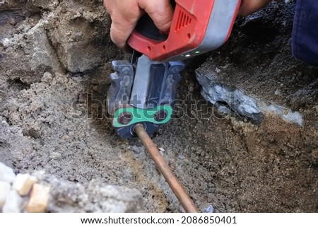Hands of a plumber fixing an underground hot water pipe leaking with a tool.