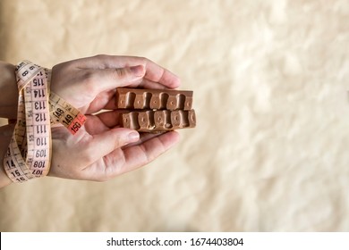 Hands Of Plus Size Woman Tied With Measuring Tape And Holding Chocolate. Weight Loss Problems. Plus Size Woman Cant Stop Unhealthy Eating