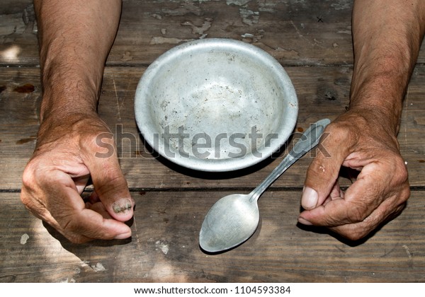hands the poor old man's and
empty bowl on wood background. The concept of hunger or poverty.
Selective focus. Poverty in retirement.Homeless. 
Alms