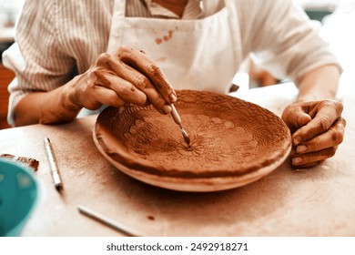 Hands, pottery and artist with knife for carving pattern or design with tools in creative workshop. Clay, equipment and person sculpting ceramic for art craft, shape or decoration for manufacturing - Powered by Shutterstock