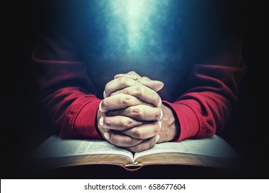 Hands in prayer over a bible.