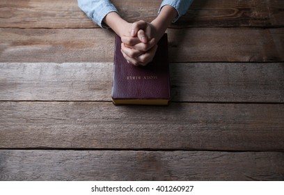 Hands Praying With A Bible In A Dark Over Wooden Table