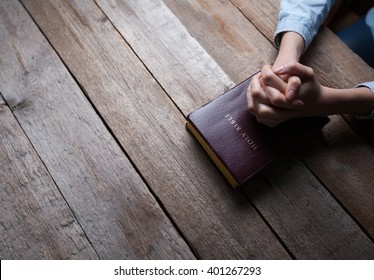 Hands Praying With A Bible In A Dark Over Wooden Table