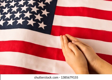 Hands of praying little girl on the background of the American flag. The concept of patriotism - Powered by Shutterstock