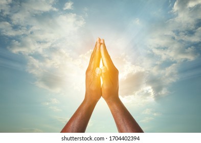 Hands of praying man against blue cloudy sky