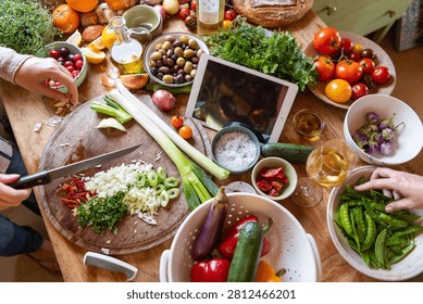 Hands preparing a colorful array of fresh vegetables on a wooden table.