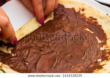 Hands preparing and rolling pancakes  with chocolate cream, close up. Sweet homemade dessert.