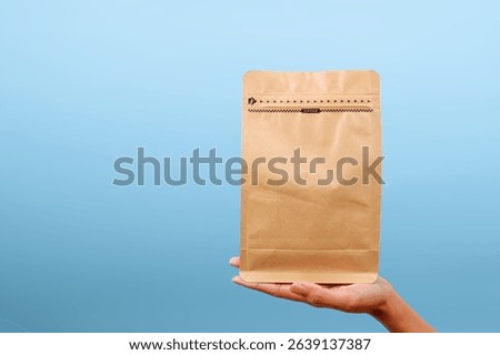 Hands Presenting Blank Brown Packaging Paper Pouch Over Blue Background