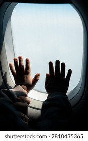 Child’s hands pressed to airplane window, capturing wonder and bright sky above clouds