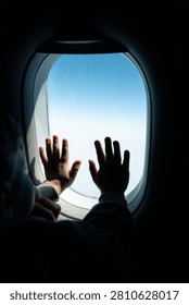 Child’s hands pressed to airplane window, capturing wonder and bright sky above clouds