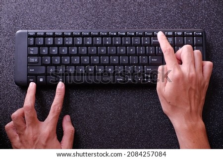 Hands pressing ctrl alt del on  computer keyboard, with black background.