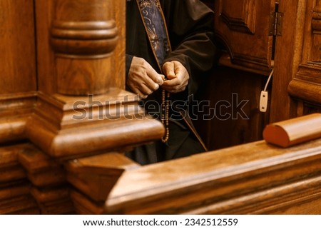 hands of a priest holding a Catholic rosary during confession in the confessional