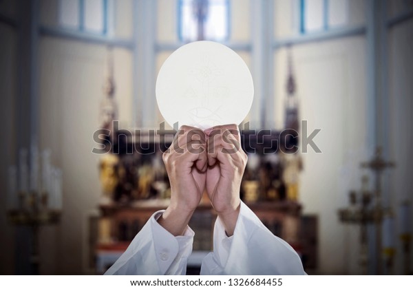 Hands of a Priest raise a communion bread while\
celebrating a mass in the\
church