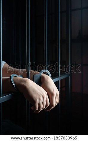 hands of prisoner with handcuff in jail as background, hands in handcuffs behind bars, man in the handcuffs is behind the bar in the police station, prisoner concept