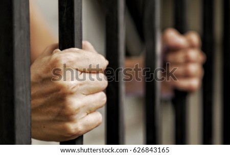 hands of prisoner holding black metal bars, criminal locked in jail waiting for release