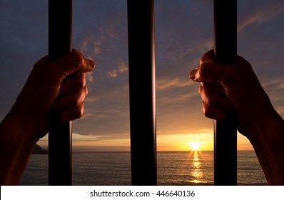 Hands of the prisoner on a steel jail close up with the sunset in the background