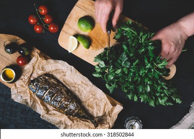 Hands In The Process Of Cooking Fish, Pepper, Parsley, Tomato, Lime On A Cutting Board On A Black Wooden Background