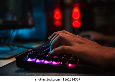 Hands of professional gamer boy playing video games on computer in dark room using backlit colorful keyboard