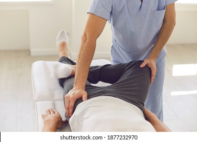 Hands Of Professional Man Chiropractor Manual Therapist In Blue Medical Uniform Fixing Man Patients Pelvic Bones During Visit At Rehabilitation Theapy In Manual Therapy Clinic. Osteopath During Work