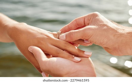 Hands, proposal and engagement ring at lake outdoors for couple, marriage and wedding. Commitment, love and jewelry of woman and man proposing and putting band on finger for trust, care and romance. - Powered by Shutterstock