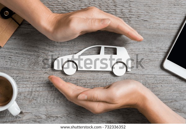 Hands protecting icon of car over wooden table.\
Top view of hands showing gesture of protecting car. Car insurance\
and automotive business\
concept.