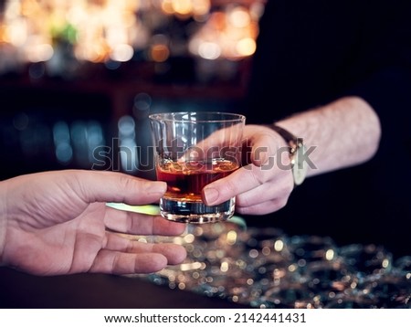 Hands of a pub customer and bartender serving a glass of neat whiskey. Close up view.