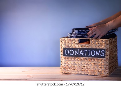 Hands Putting A Blanket In A Box For Clothing Donations On A Blue Background. Charity And Donation Concept. Copy Space.