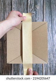 Hands Putting Brown Paper Tape On Box