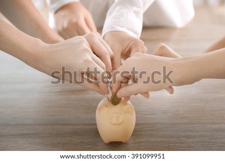 Hands putting coin into piggy bank at the table
