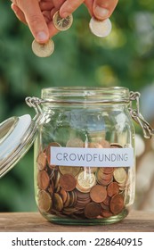 Hands putting coins in a money jar full of coins with the word crowdfunding on it.