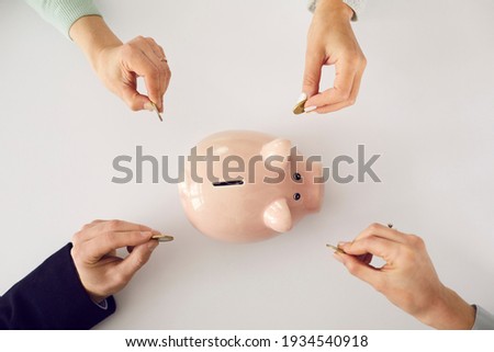 Hands putting money in pink piggy bank on white table background. People saving up together, family household income, opening account, banking, joint venture, economy concept. High angle, from above