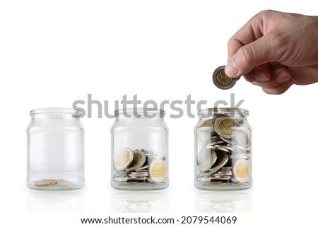 Hands are putting in more coins. Glass bottles with growing coins are like a diagram of savings ideas. White isolated background